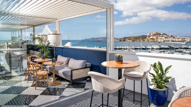 A rooftop terrace with outdoor seating, a view of the sea, and a distant town. - Ocean Drive Ibiza (Ibiza Town)