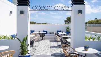 Un espacio al aire libre con mesas y sillas, plantas en macetas y un letrero que dice 'ocean drive'.
