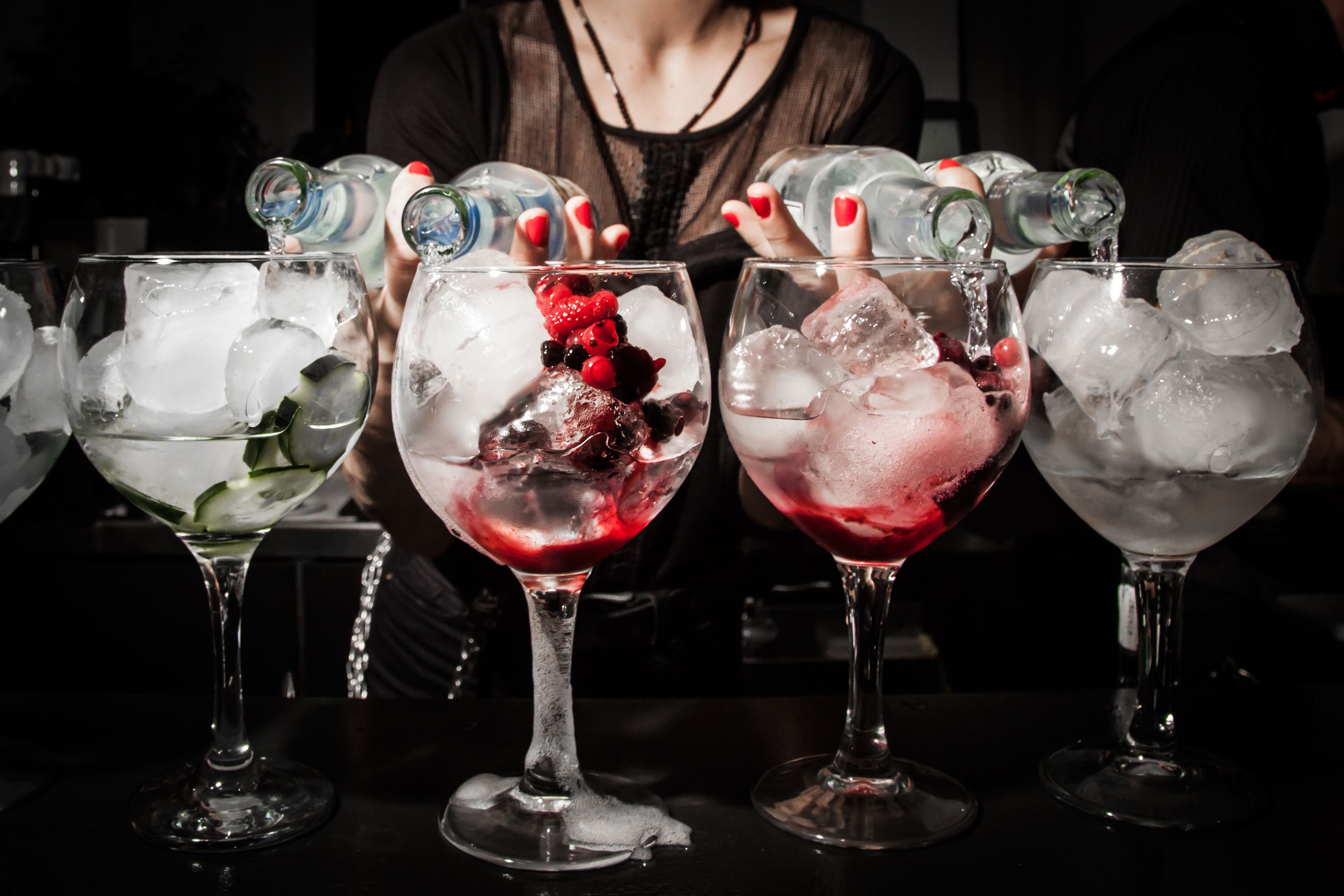 Drei Gläser mit Eisgetränken, Eiswürfeln und Beeren, sowie eine Person, die Wasser in eine Flasche gießt.