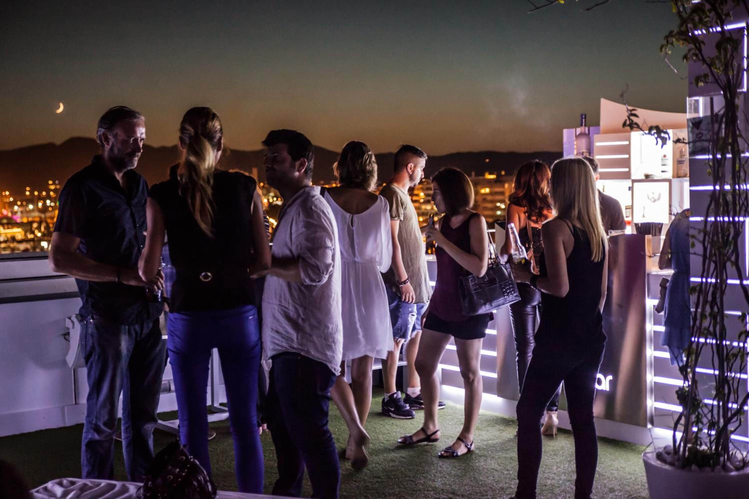 A group of people standing on a rooftop terrace with a cityscape view in the background.