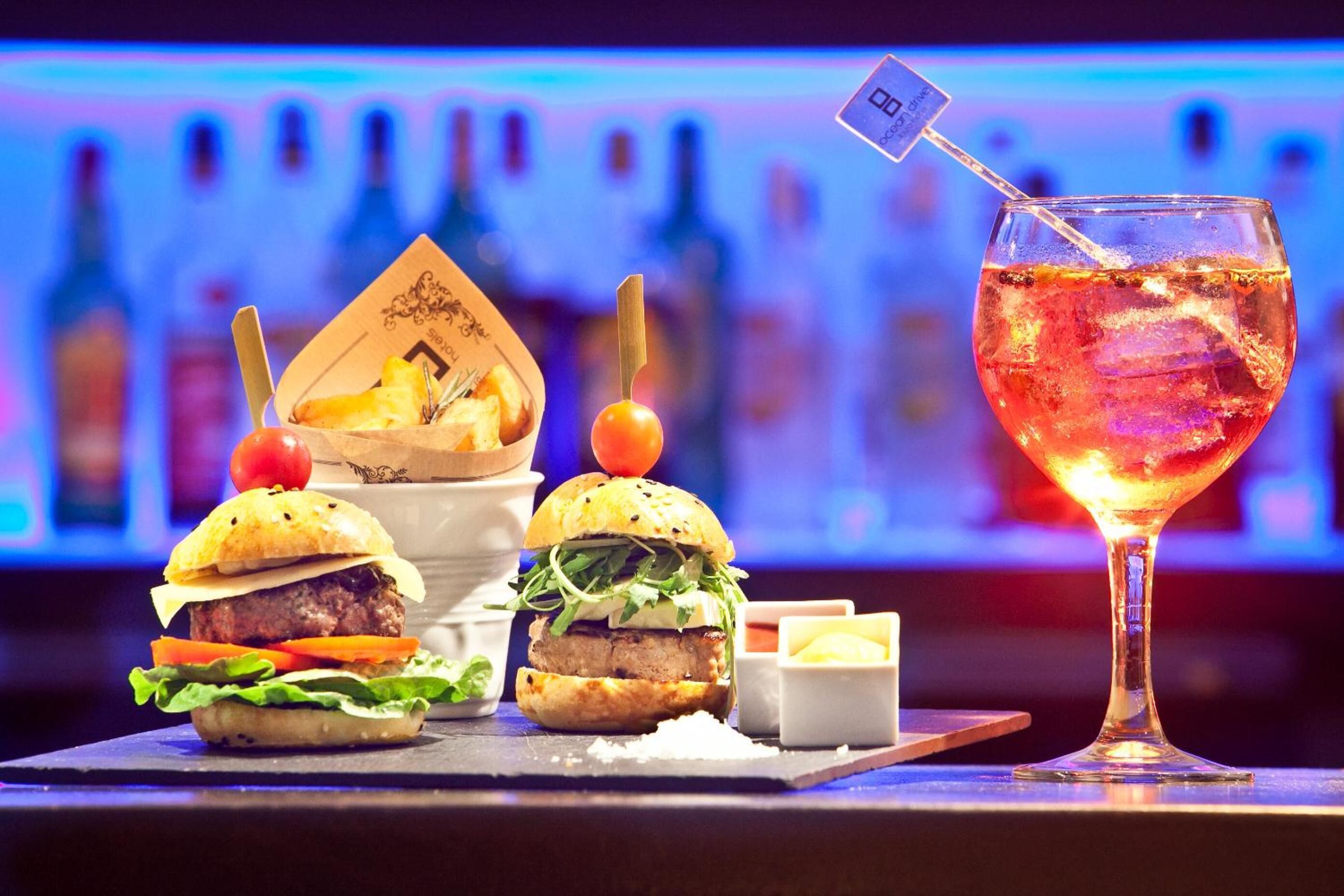 A bar setting with two burgers and a cocktail glass.