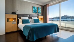 A modern hotel room with a large bed, two nightstands, a view of the sea, and a cityscape. - Ocean Drive Ibiza (Ibiza Town)