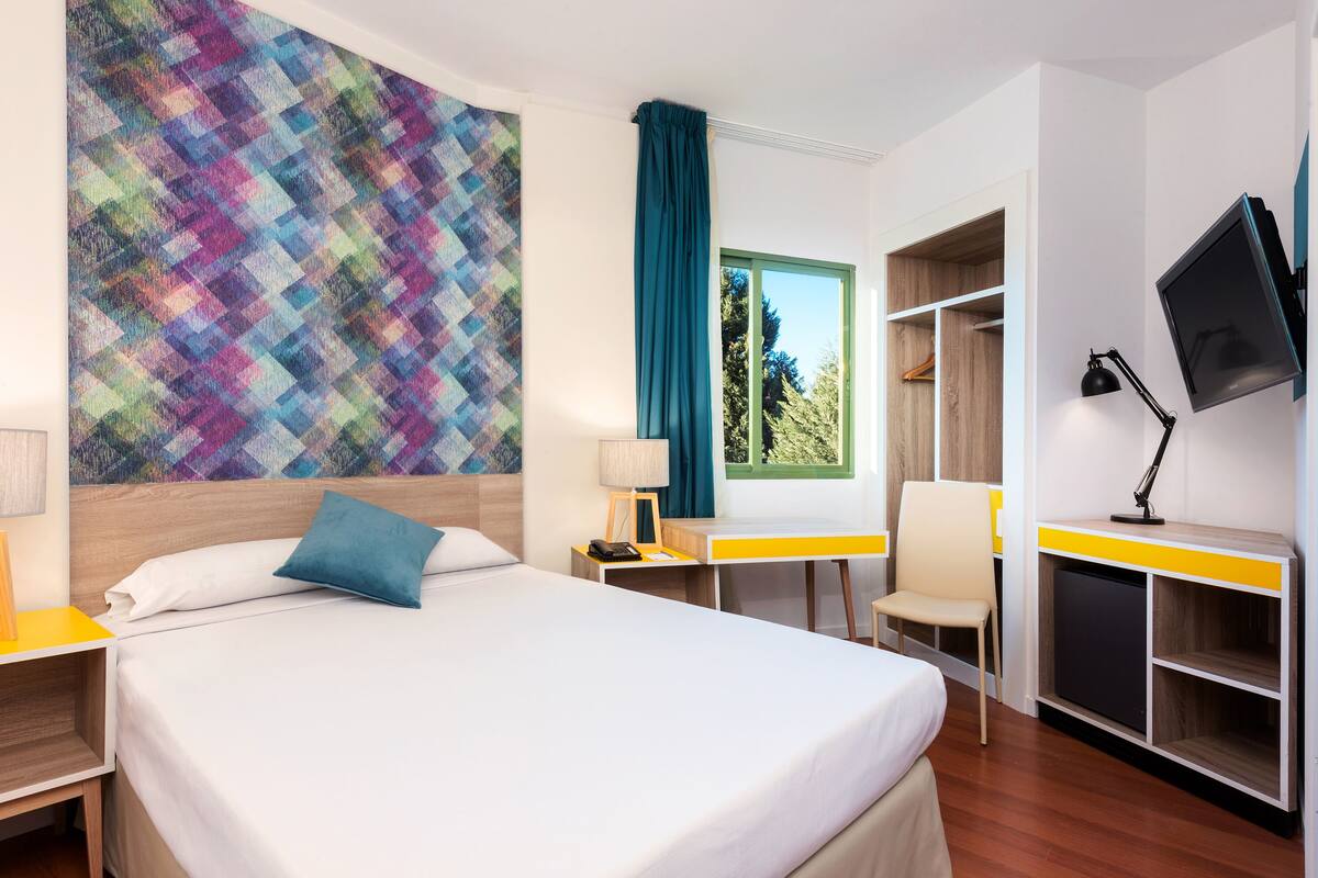 Ein Hotelzimmer mit Bett, Schreibtisch, Stuhl, Fernseher und Kleiderschrank.
