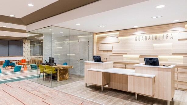 A modern reception area with a glass partition, wooden reception desk, and a sign that reads "GUADALAJARA".