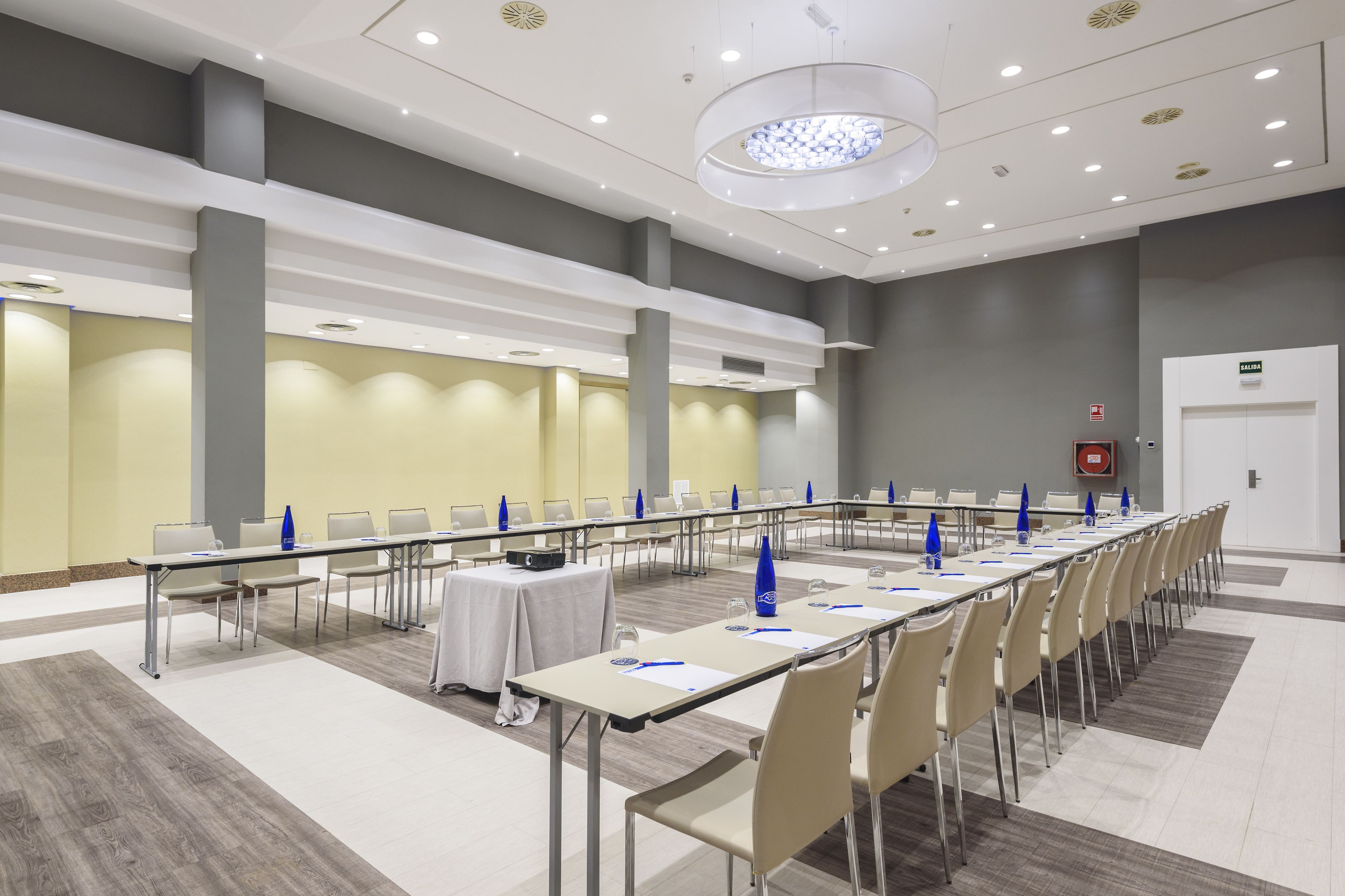 Un salón de conferencias con mesas largas, sillas e iluminación empotrada en el techo blanco.