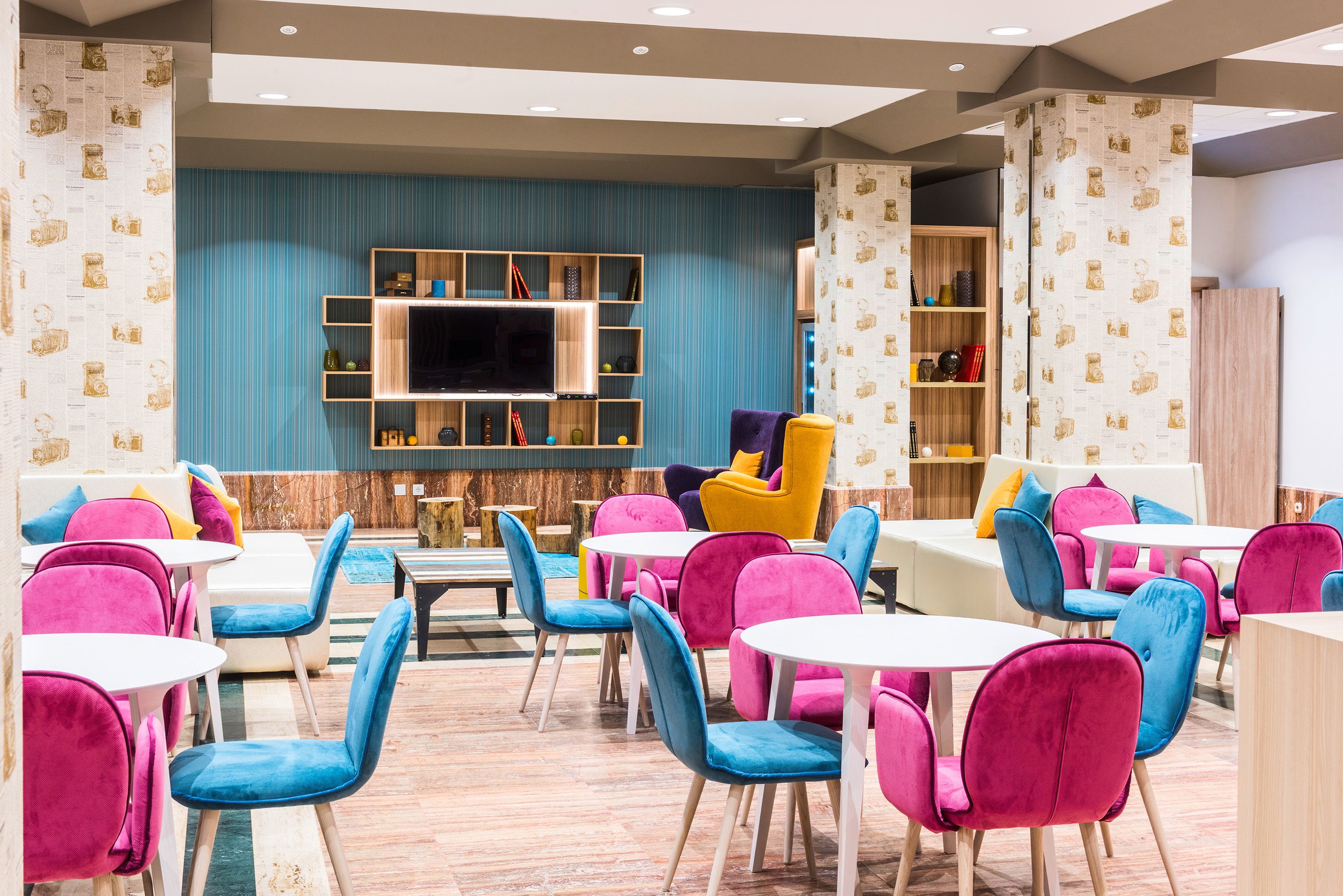 A brightly lit indoor space with multiple seating areas, including tables and chairs, and a television mounted on the wall.