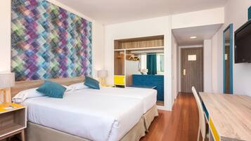 Une chambre d’hôtel avec un grand lit, un bureau et une télévision. Un tableau coloré orne le mur, et un miroir est placé au-dessus du lit.