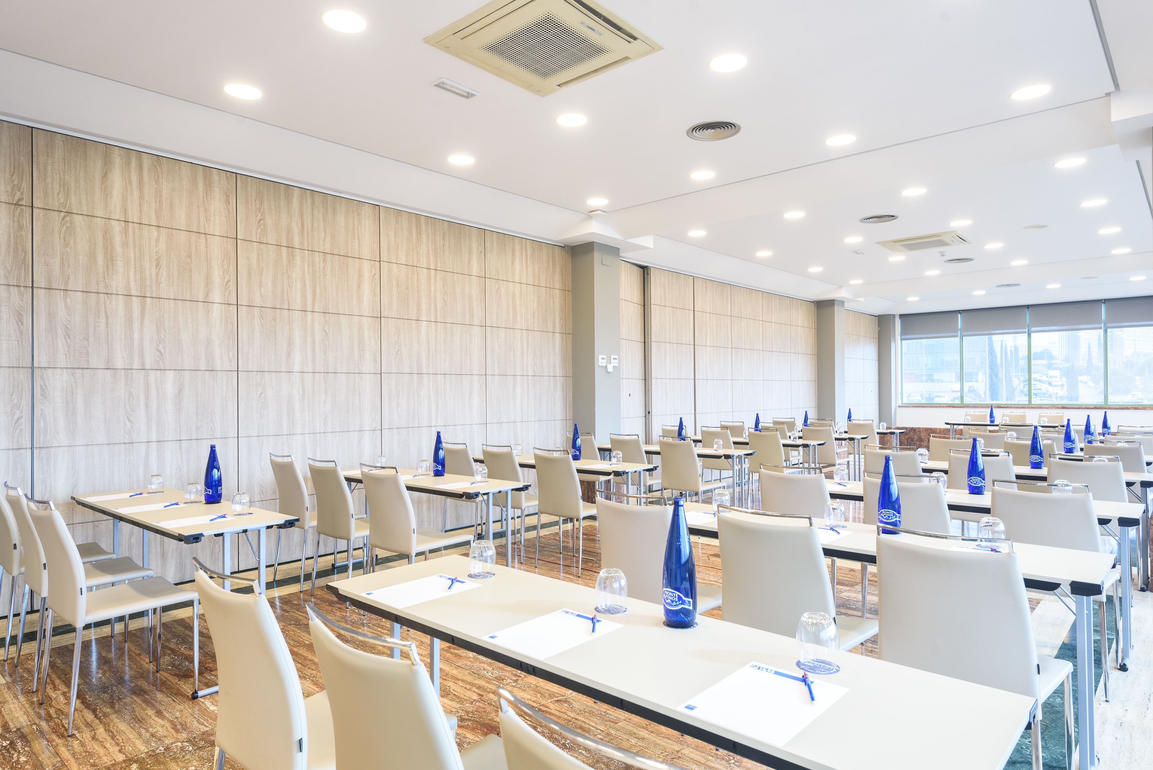 A conference room with rows of tables and chairs, equipped with water bottles and pens.
