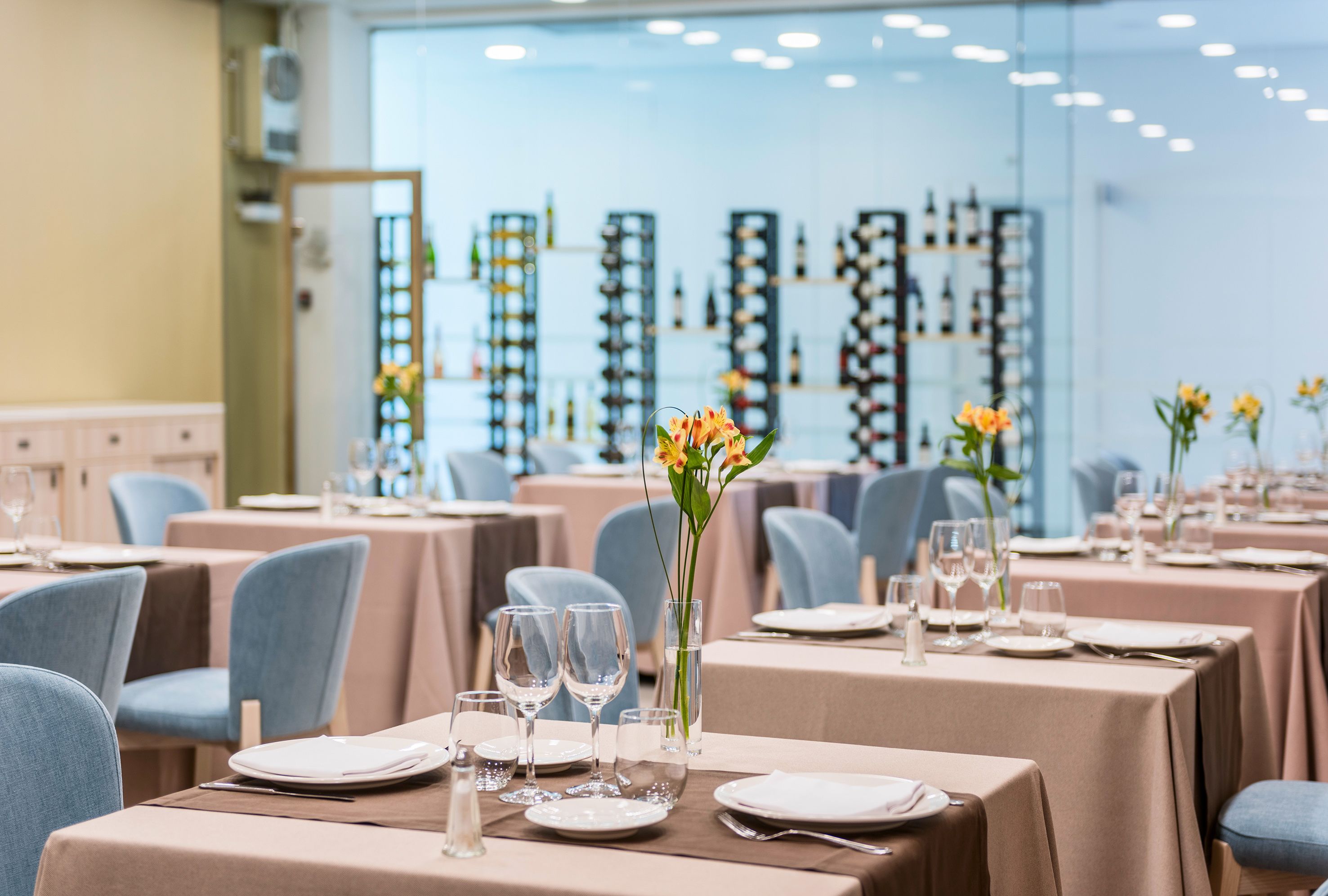 A restaurant with tables set for dining, featuring a wine rack in the background.
