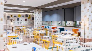 A spacious dining area with multiple tables and chairs, a clock on the wall, and a patterned wallpaper design.