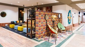 A modern lobby with a brick-patterned partition, yellow and blue seating, a green chair, and a patterned rug.