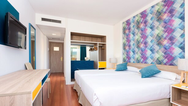 Una habitación de hotel con una cama, un escritorio, un televisor y una pared de colores.