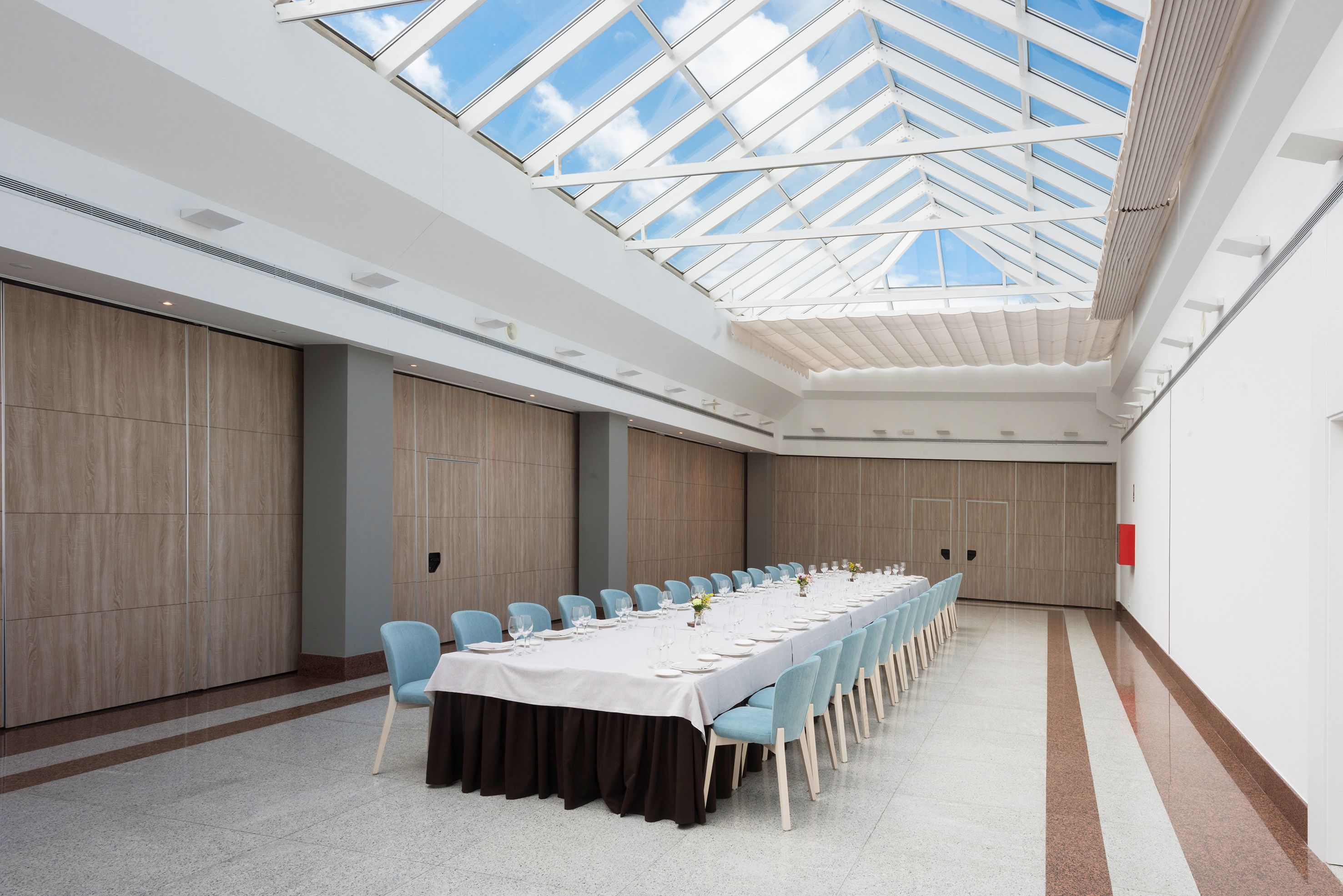 A conference room with a long table, light blue chairs, and a high ceiling with a skylight.