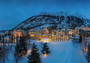 A snow-covered mountain town at dusk with illuminated buildings and a clear sky.