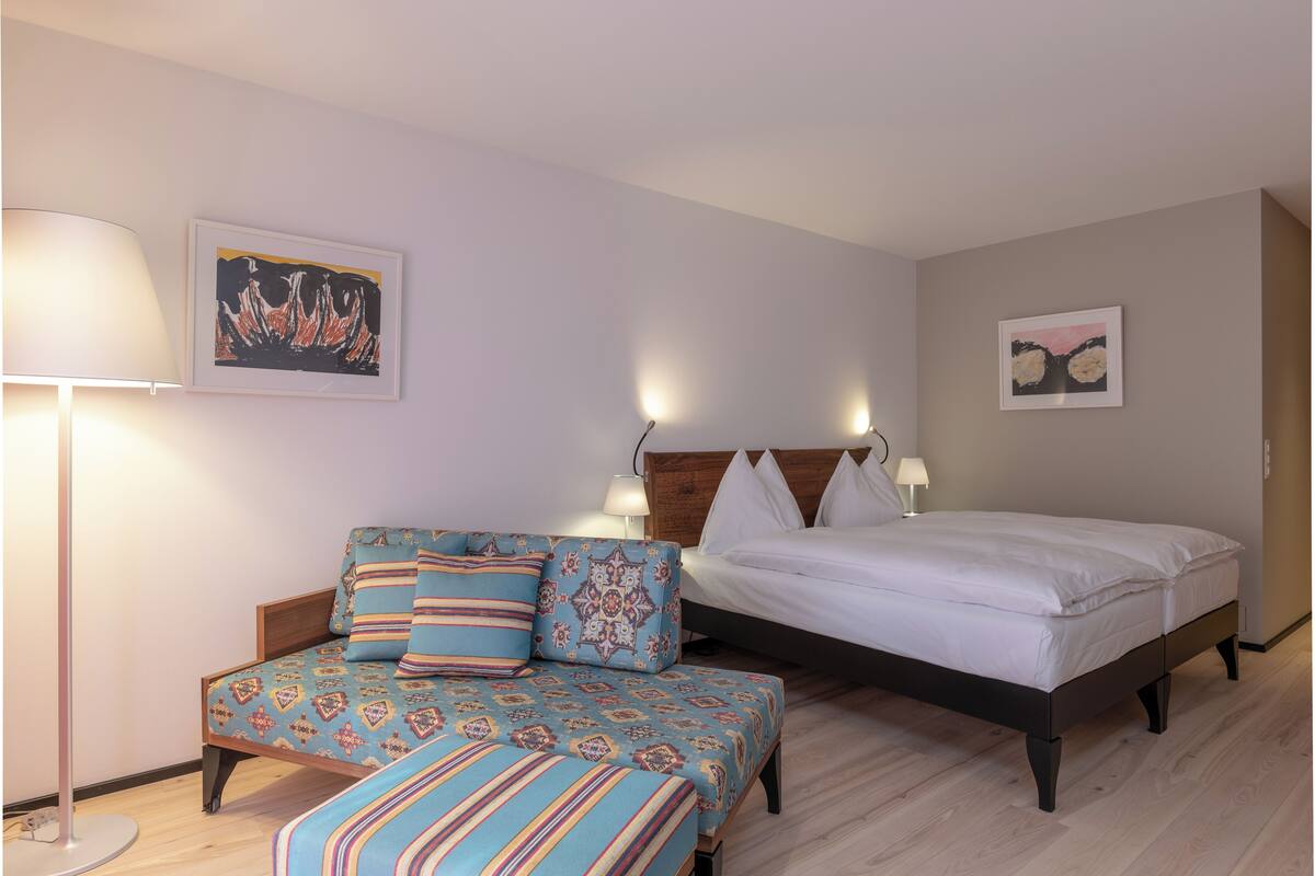 A bedroom with a bed, a sofa, and two wall-mounted lamps.