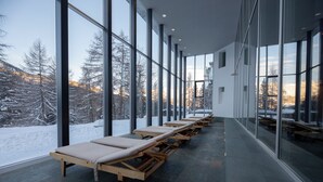 Una fila de tumbonas de madera con ruedas, dispuestas a lo largo de un pasillo con ventanas amplias que dan a árboles cubiertos de nieve.