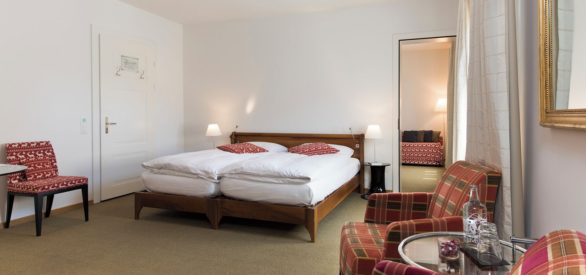 A hotel room with a bed, two chairs, a small table, and a mirror.
