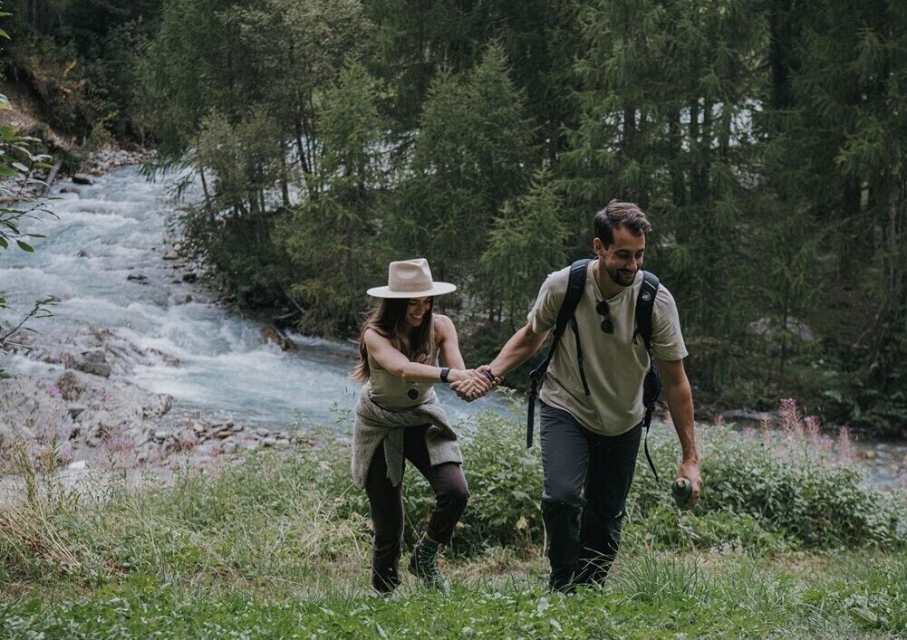 Deux personnes se promènent le long d’une berge, dans une zone boisée.
