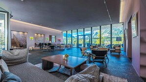 Un amplio y moderno salón con asientos cómodos, una escalera y grandes ventanales con vistas a la montaña.