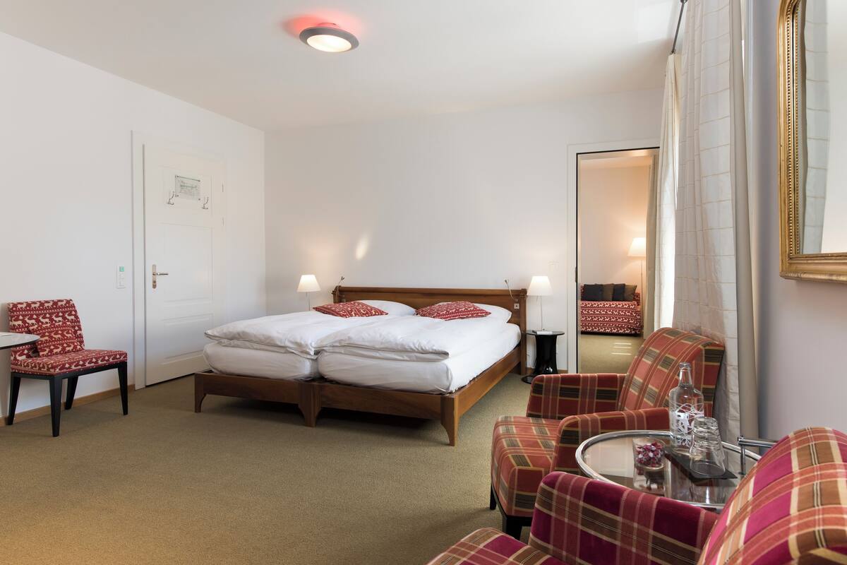 A hotel room with a bed, two chairs, a small table, and a mirror.