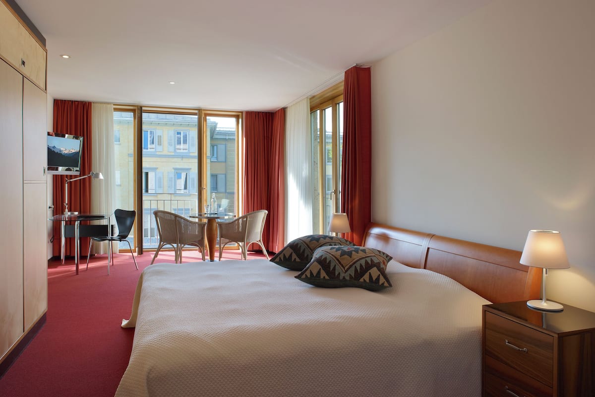 Una habitación de hotel con una cama, un escritorio, una silla, un televisor y ventanas amplias.