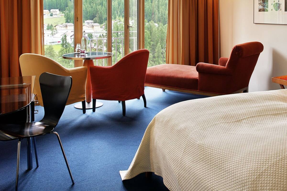 A hotel room with a bed, a chair, a table, and a view of the outside.