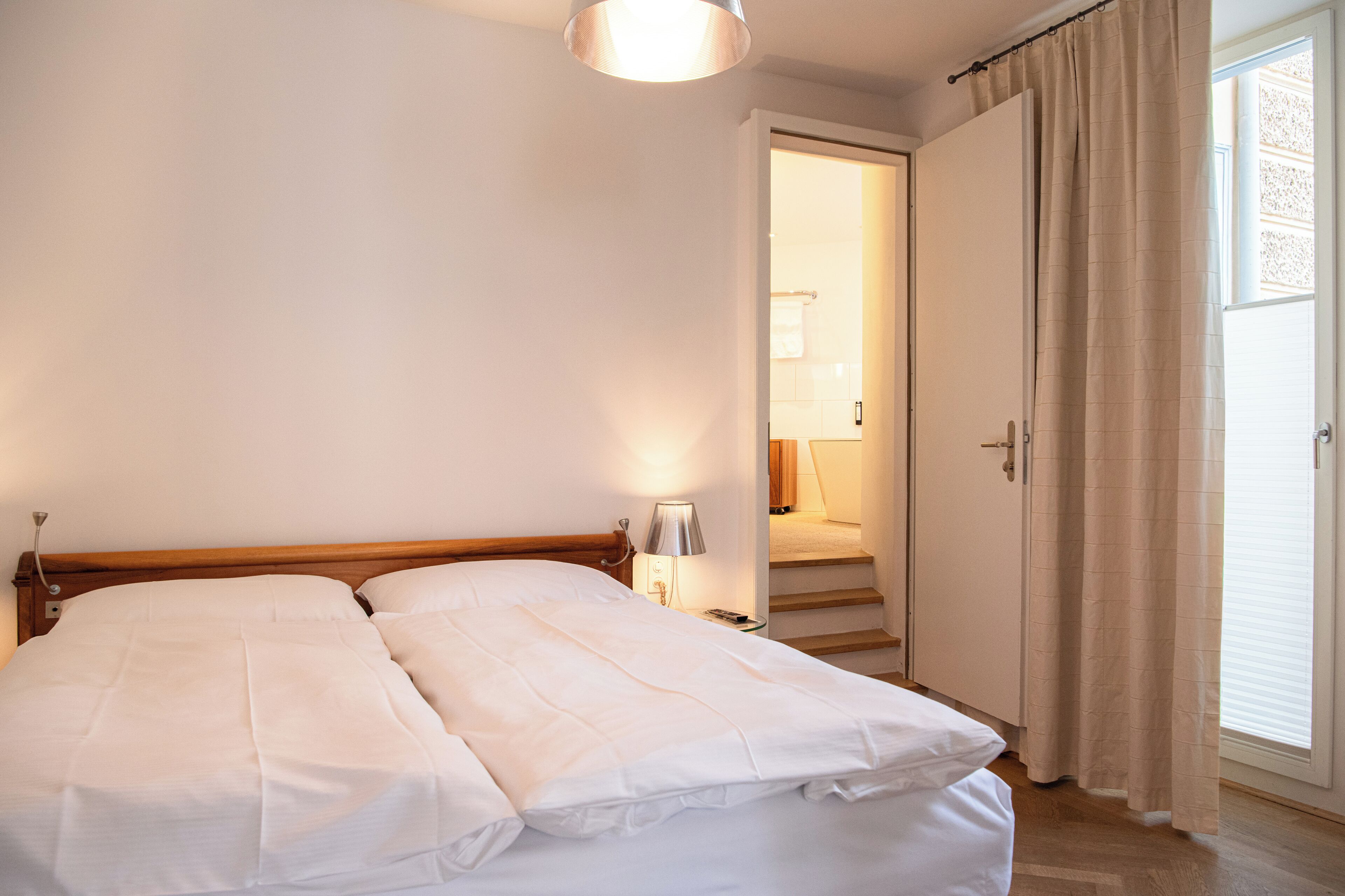 Una cama doble con ropa de cama blanca, una lámpara de noche y un cabecero de madera.
