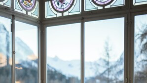 Un comedor con una mesa dispuesta para dos personas, una ventana con vistas a montañas nevadas y una silla de mimbre.