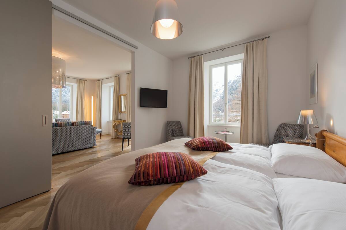 A hotel room with a large bed, a TV mounted on the wall, a window with curtains, and a view of the outdoors.