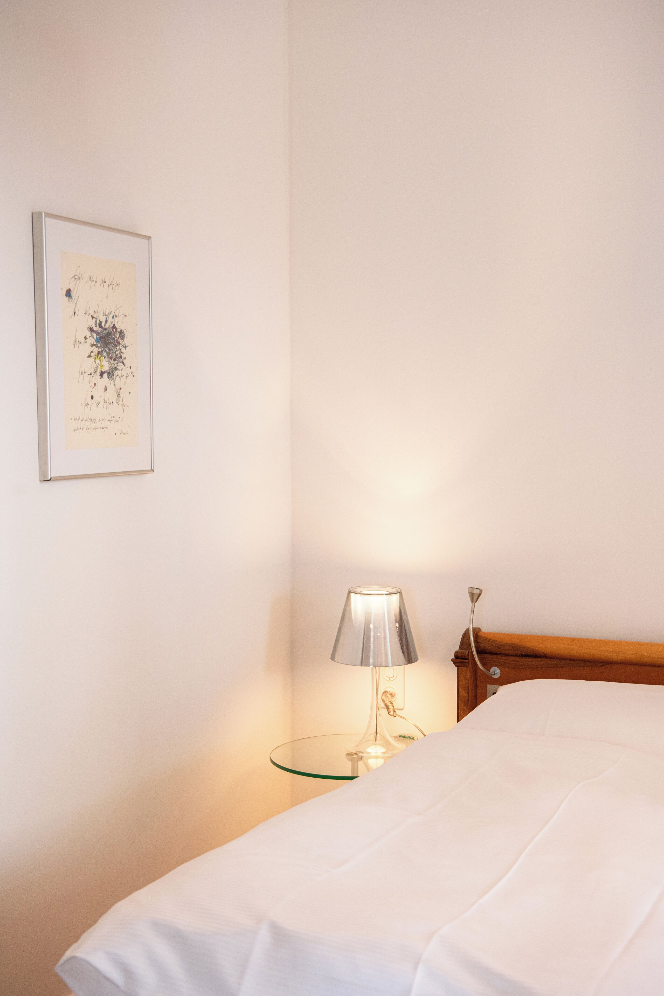 A neatly made bed with white linens, a bedside lamp, and a framed artwork on the wall.