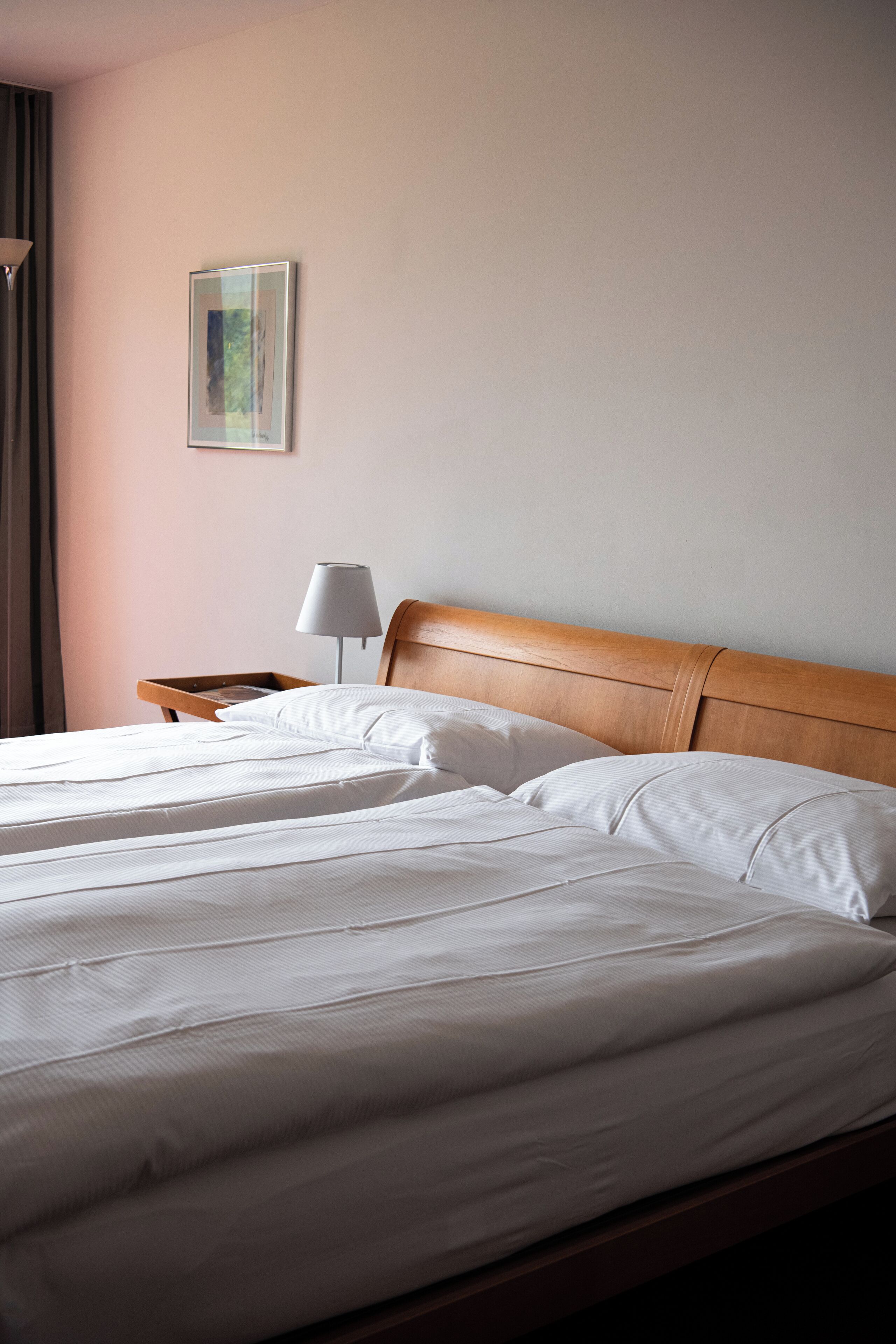 Habitación de hotel con cabecera de madera, cama con ropa blanca, mesita de noche con lámpara y un cuadro enmarcado en la pared.