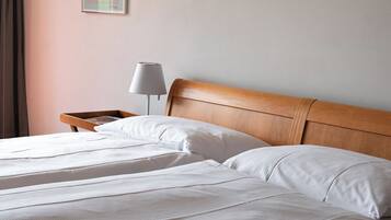 Habitación de hotel con cabecera de madera, cama con ropa blanca, mesita de noche con lámpara y un cuadro enmarcado en la pared.
