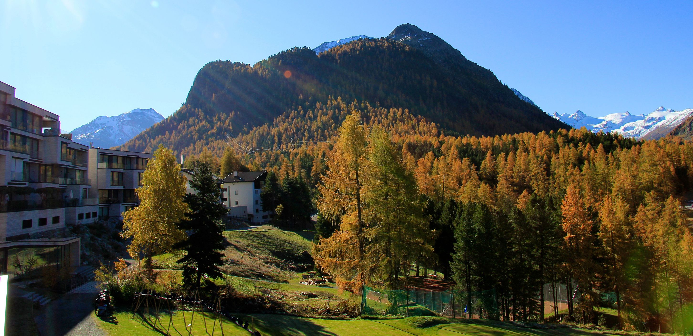 A mountainous landscape with a building surrounded by trees and a clear sky.