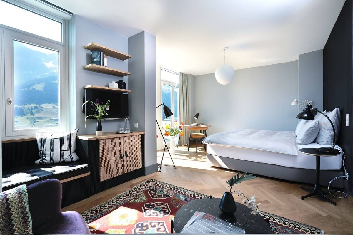 A modern room with a bed, a desk, a TV, and a view of the outdoors.