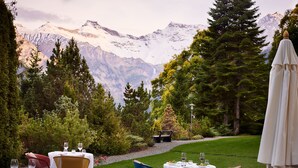 A restaurant with outdoor seating overlooking snow-capped mountains, surrounded by greenery. - Bellevue Parkhotel & Spa - Relais & Châteaux (Adelboden)