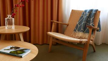 A wicker chair with a blue and white patterned throw blanket, a clear glass vase with red berries, and a book on a round wooden table.