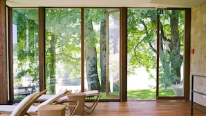A spacious room with large glass doors leading to a garden, wicker chairs, and a wooden floor. - Bellevue Parkhotel & Spa - Relais & Châteaux (Adelboden)