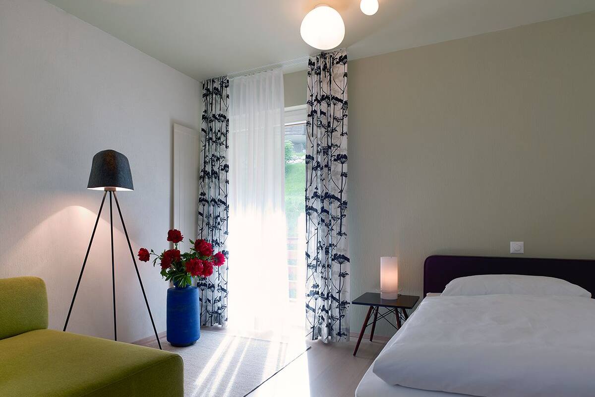 A hotel room with a bed, a desk with a lamp, a chair, and a vase with flowers.