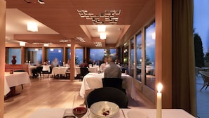 A restaurant with tables set for dining, a candle on the table, and a view of the outdoors. - Bellevue Parkhotel & Spa - Relais & Châteaux (Adelboden)