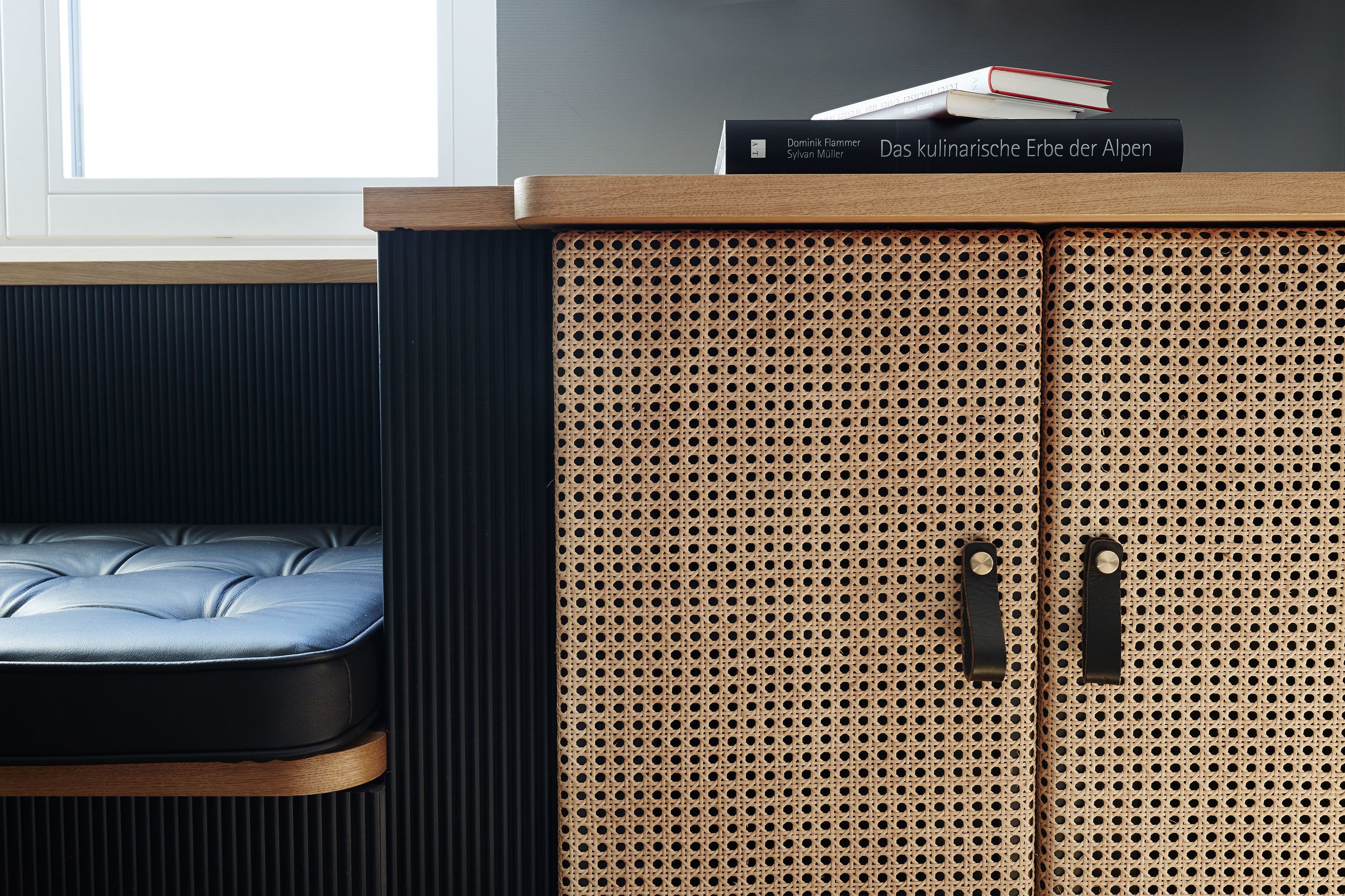 A room with a blue leather bench, a wooden cabinet with perforated panels, and a window in the background.