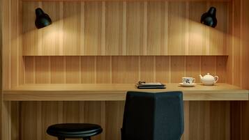 A wooden wall with two black wall sconces, a white teapot, a cup, and a notebook on a shelf.