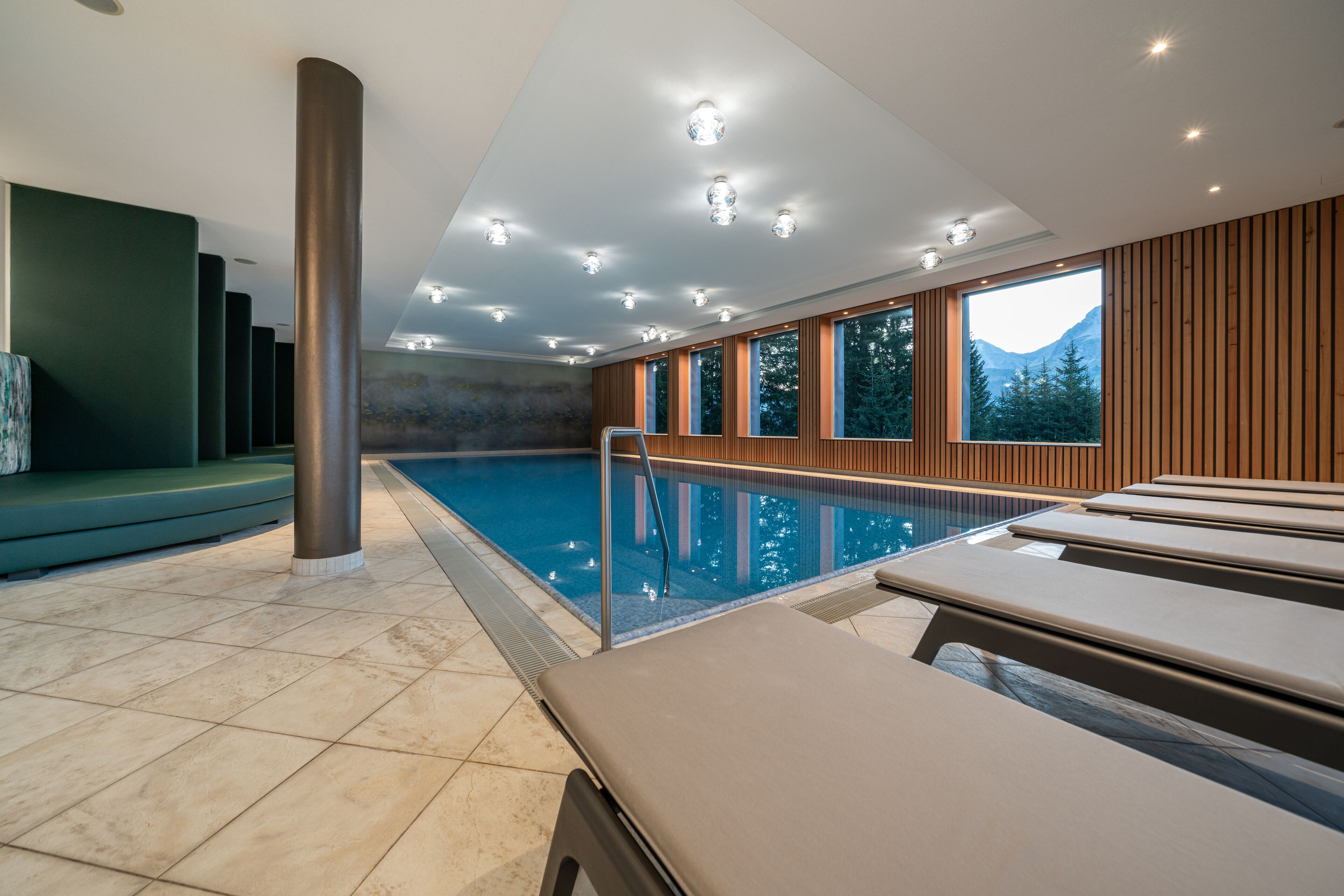 Una piscina interior moderna con vistas a montañas, paneles de madera y una zona de estar.