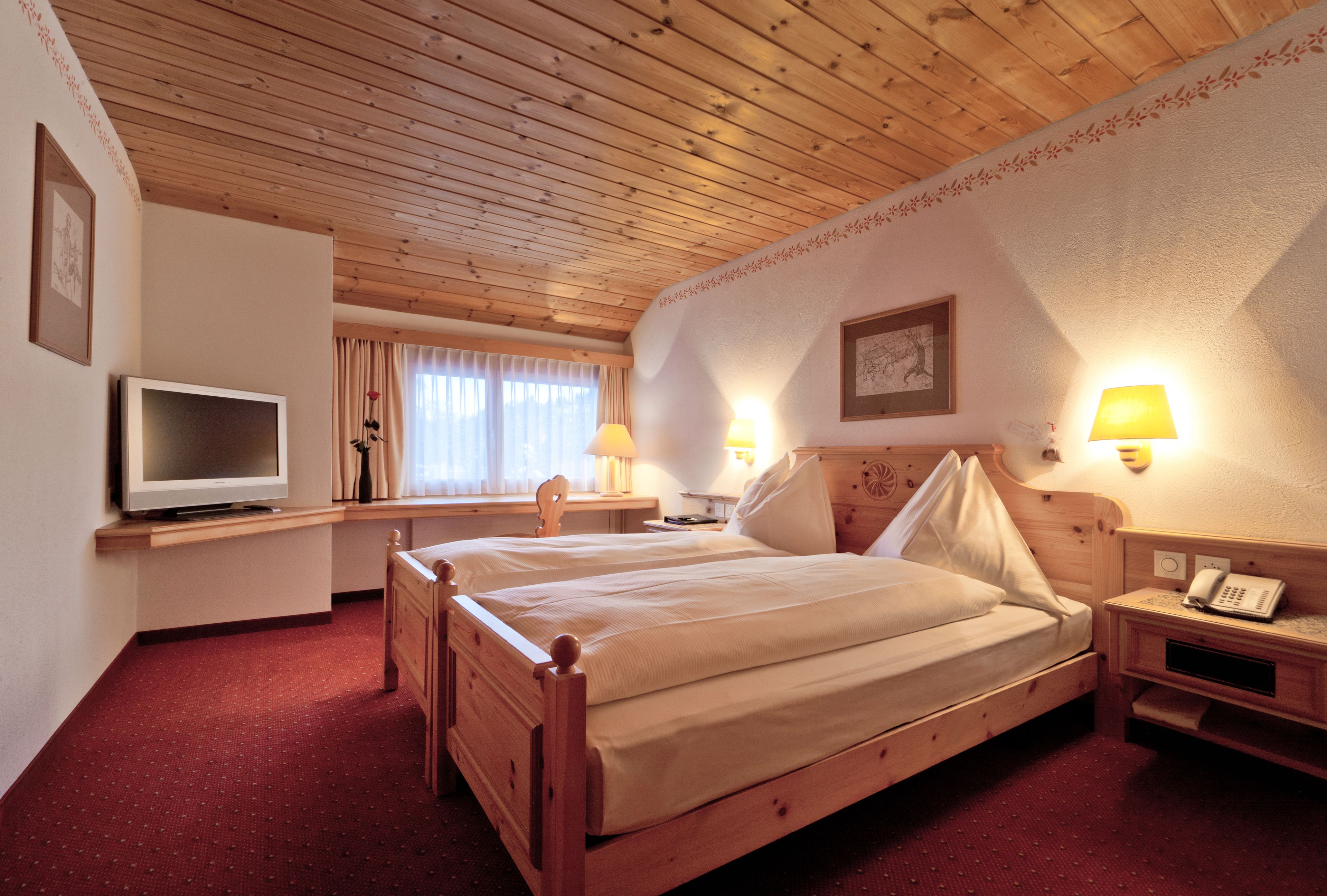 A wooden-paneled room with two beds, a desk, a television, and wall-mounted lamps.