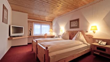 A wooden-paneled room with two beds, a desk, a television, and wall-mounted lamps.