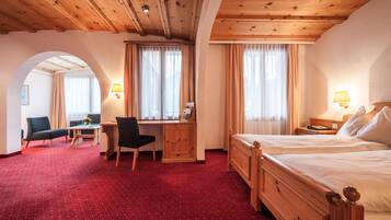 A hotel room with a wooden ceiling, two beds, a desk with a chair, and a red carpeted floor.