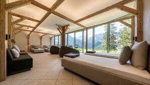 Una habitación amplia con techo alto, vigas de madera, un ventanal con vistas a la montaña, un sofá y una cama.