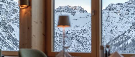 A dining table with a candle, a window with a view of snow-covered mountains.