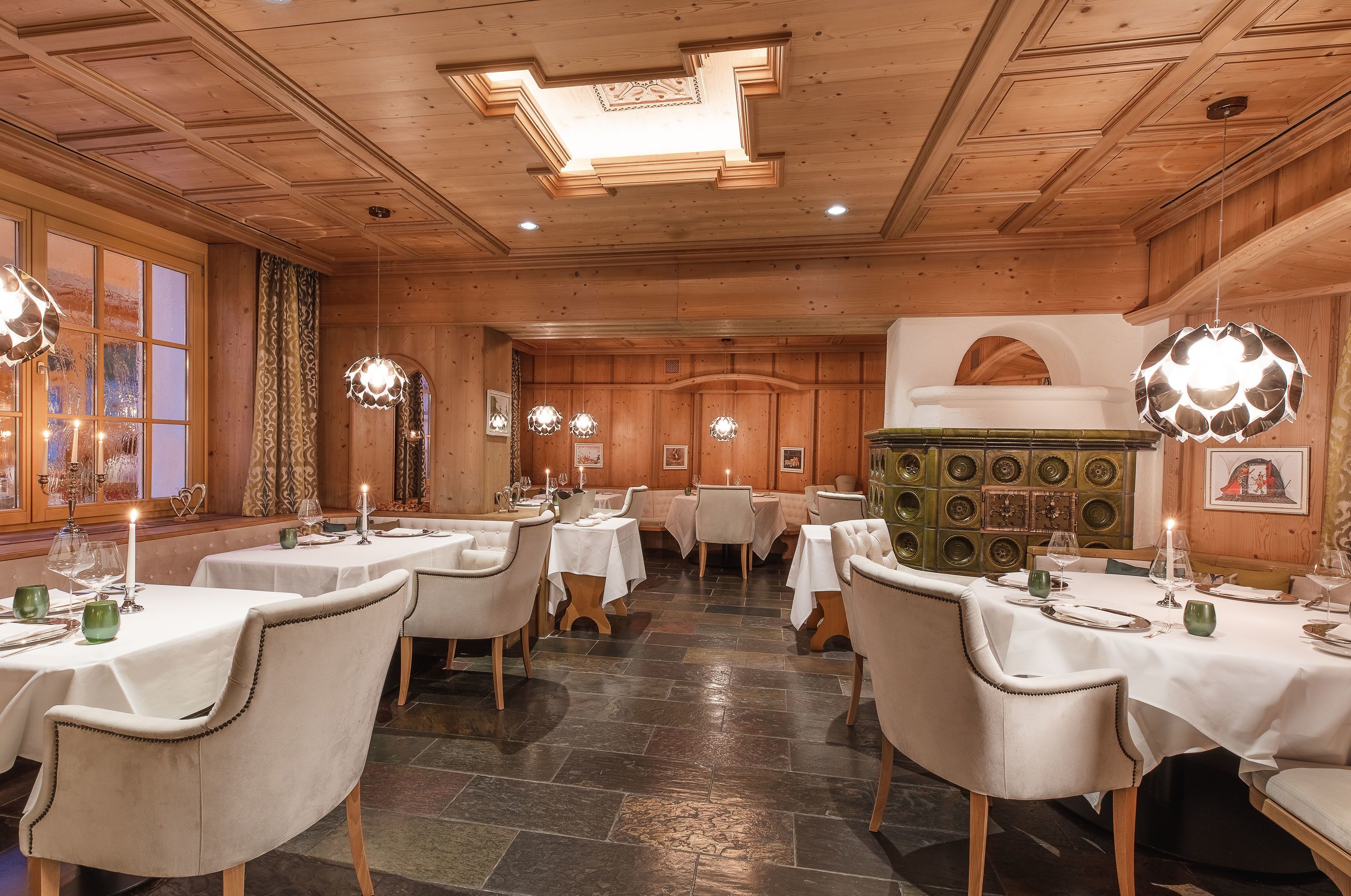 A restaurant with wooden paneling, stone flooring, and white tablecloths. Tables are set with candles and glassware.