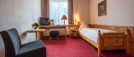 A hotel room with a wooden bed, a desk with a computer, a chair, a small table, and a lamp.