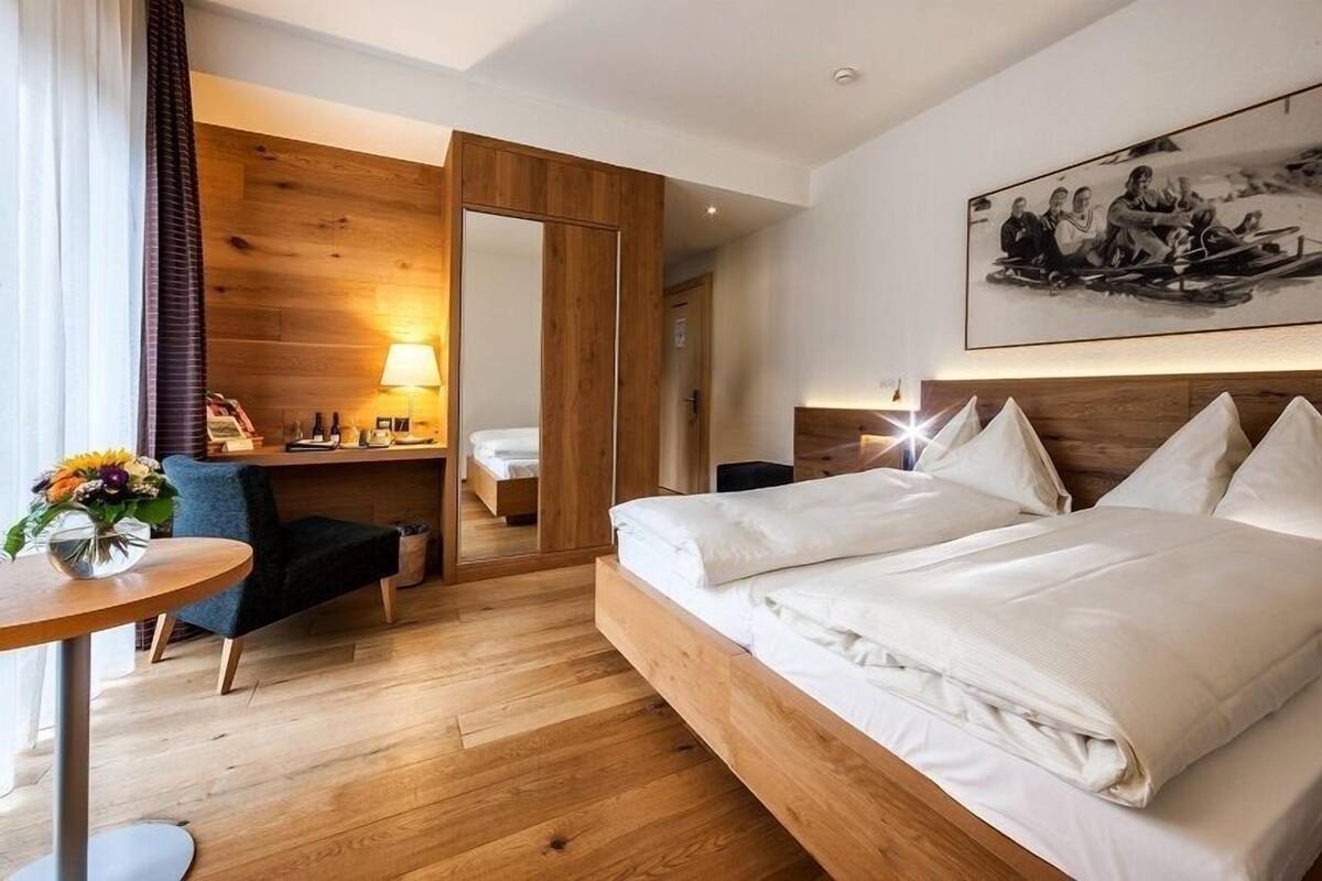 A hotel room with a large bed, a desk with a lamp, a chair, and a wooden wall panel.